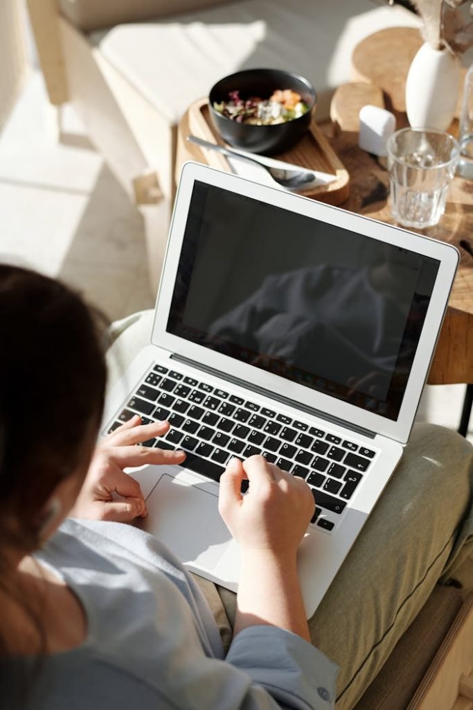 Young woman working on a laptop with a healthy breakfast beside her in a cozy setting. Ideal for lifestyle and remote work themes.